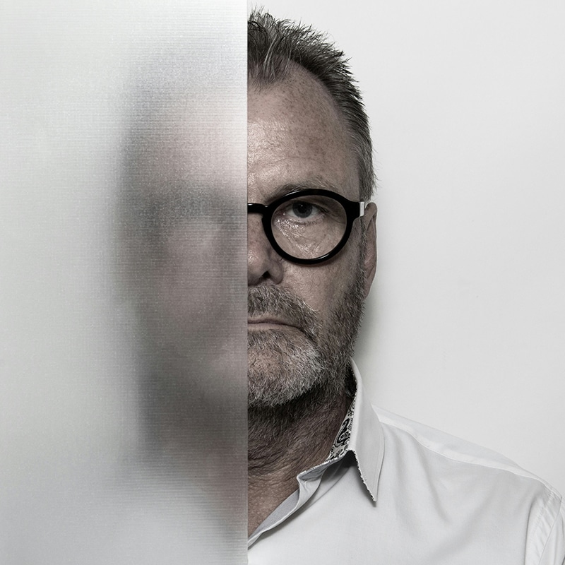 Portrait of a man with half his face sharply visible and half obscured behind frosted glass